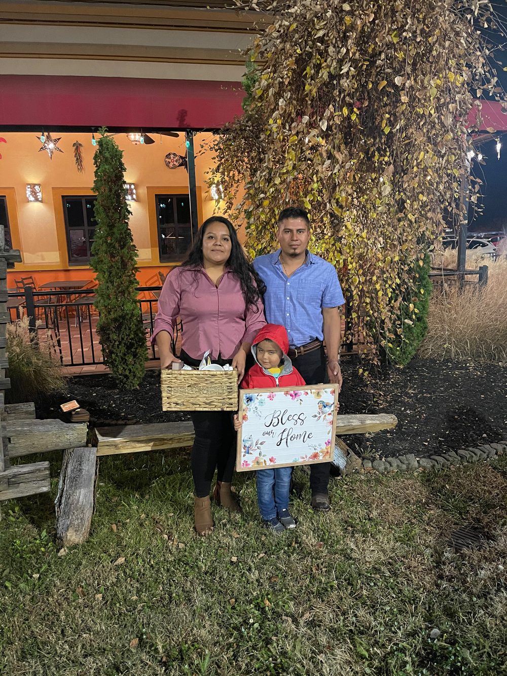 Family with their child holding a 'Bless our home' sign outside at dusk