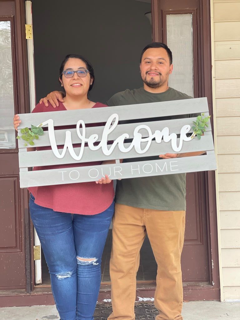 Couple holding a 'Welcome to our home' sign at their front door