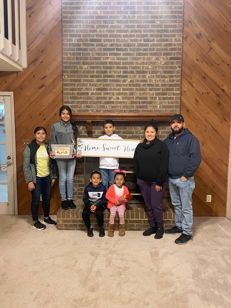 Family with their children holding a 'Home Sweet Home' sign by the fireplace of their new home