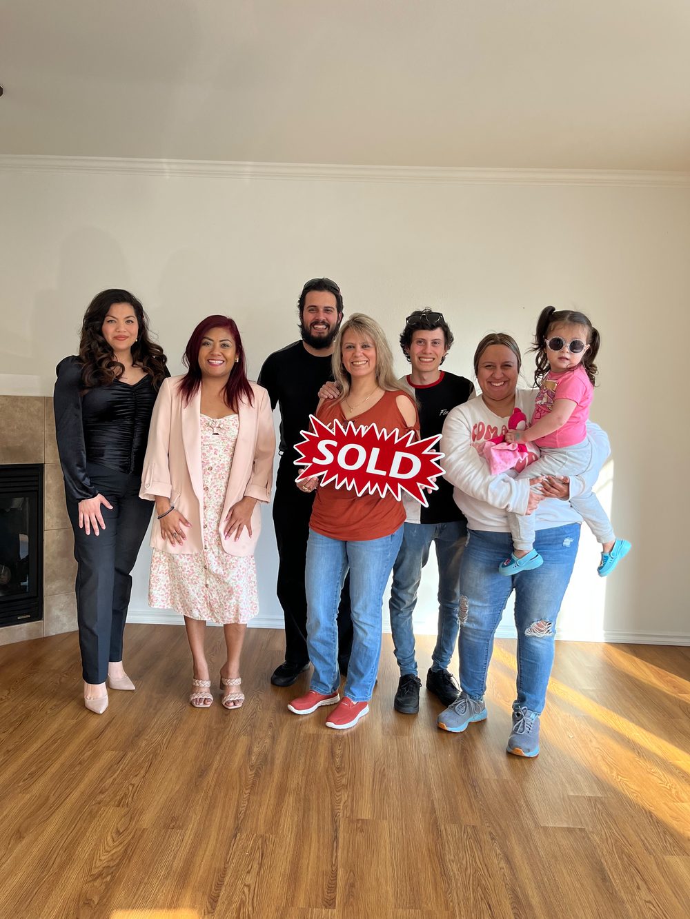 Family and friends holding a SOLD sign in their new living room