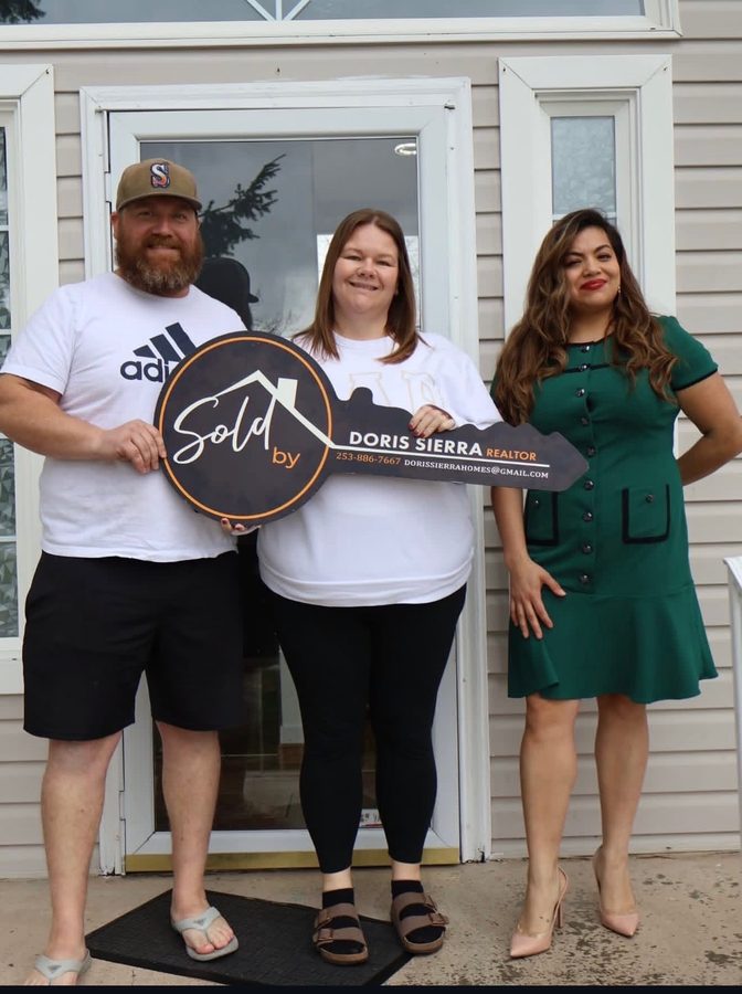 A couple and their Realtor holding a Sold by Doris Sierra key sign at the front door of their new home