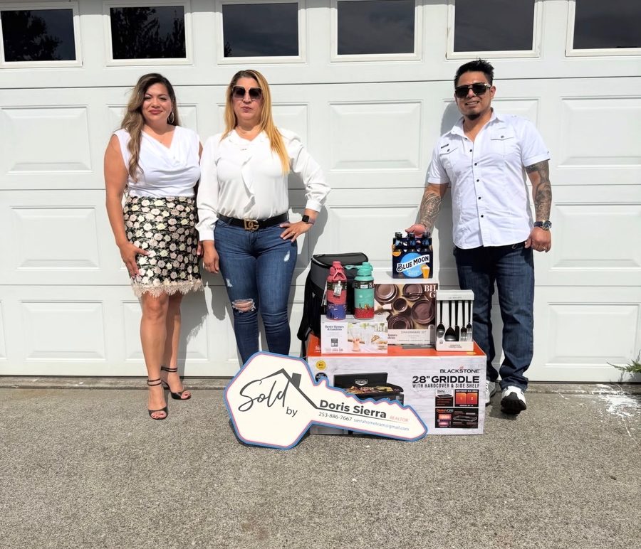 A couple and their Realtor in front of their new home's garage, surrounded by housewarming gifts