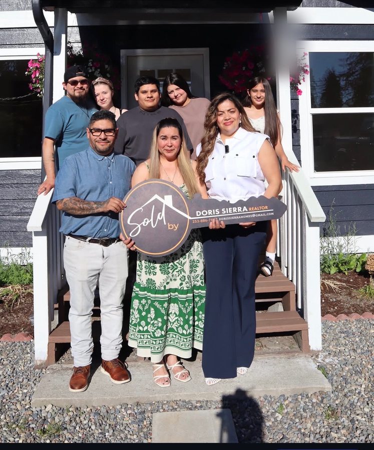 A large family gathered on the front porch of their new home, holding a Sold by Doris Sierra key sign
